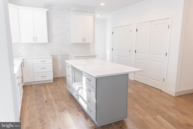 kitchen with white cabinets, decorative backsplash, light hardwood / wood-style flooring, and a kitchen island