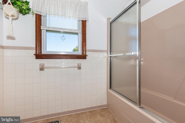 bathroom with tile walls, combined bath / shower with glass door, and tile patterned floors