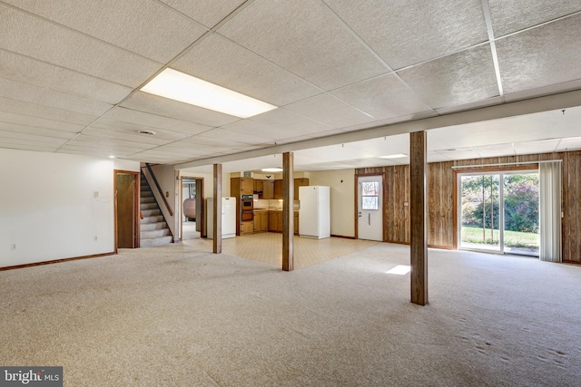 basement featuring wooden walls, white fridge, light colored carpet, and a paneled ceiling