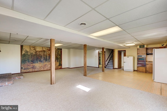 basement featuring white fridge and a paneled ceiling