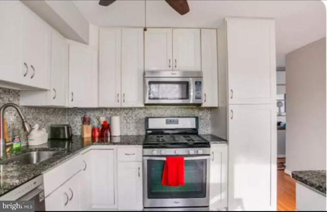 kitchen featuring white cabinets, backsplash, dark stone counters, light wood-type flooring, and stainless steel appliances