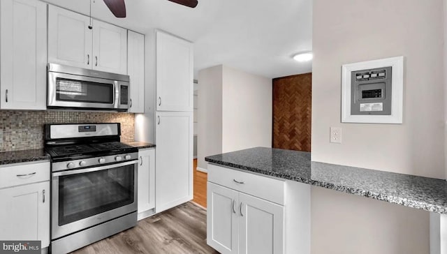 kitchen featuring tasteful backsplash, appliances with stainless steel finishes, white cabinetry, dark stone counters, and dark wood-type flooring