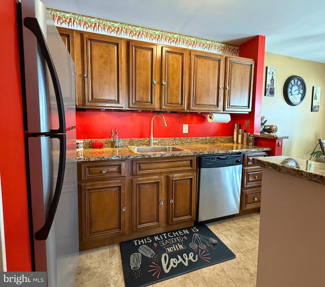 kitchen with appliances with stainless steel finishes, light tile patterned floors, dark stone countertops, and sink