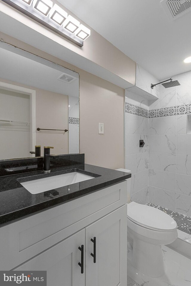 bathroom featuring toilet, vanity, and tiled shower