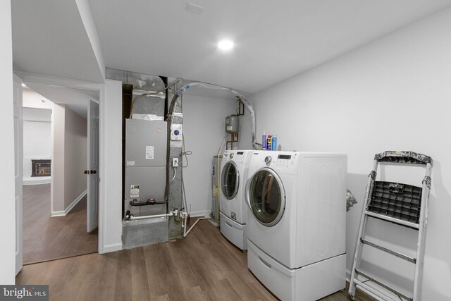 clothes washing area with heating unit, wood-type flooring, and washer and dryer