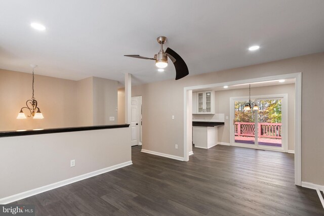 unfurnished living room with ceiling fan with notable chandelier and dark hardwood / wood-style flooring