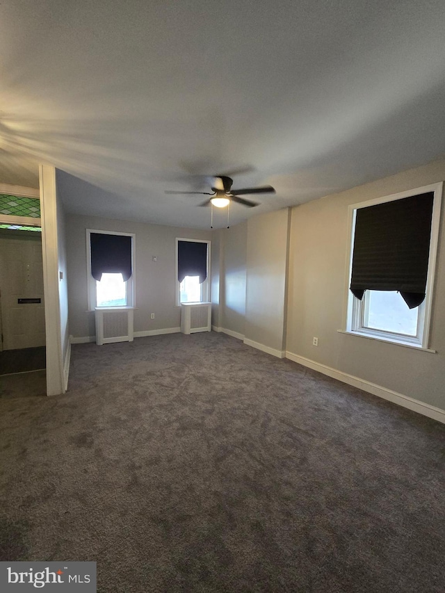 carpeted spare room featuring ceiling fan, radiator, and a wealth of natural light