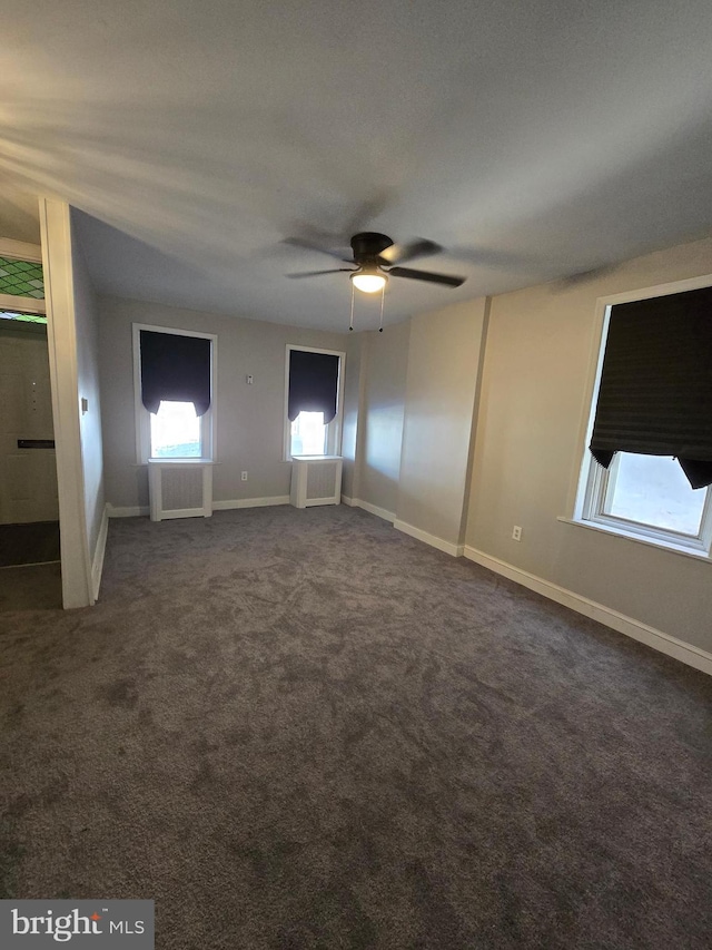 unfurnished bedroom with dark colored carpet, radiator, and ceiling fan