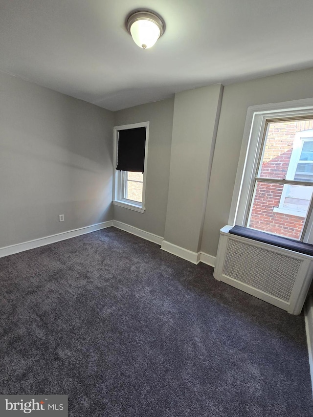 unfurnished room with radiator heating unit, a healthy amount of sunlight, and dark colored carpet