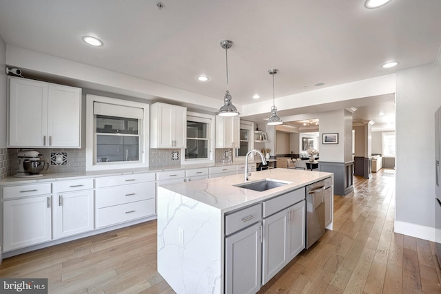 kitchen featuring a center island with sink, sink, stainless steel dishwasher, white cabinets, and light stone counters