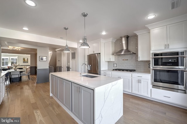 kitchen featuring white cabinetry, light stone counters, wall chimney exhaust hood, and a center island with sink