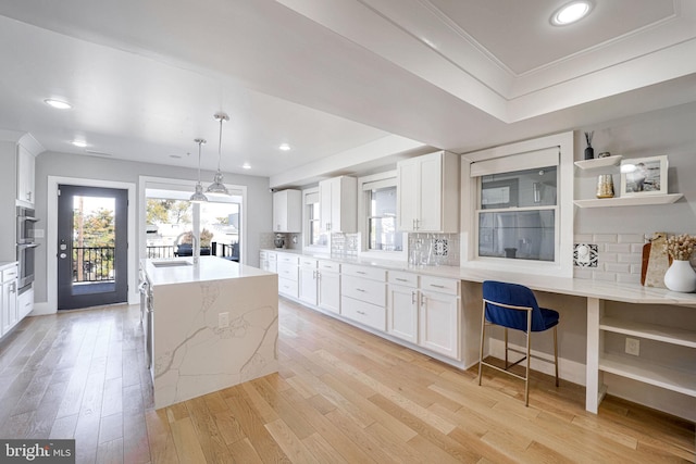 kitchen with light hardwood / wood-style floors, white cabinetry, sink, and hanging light fixtures