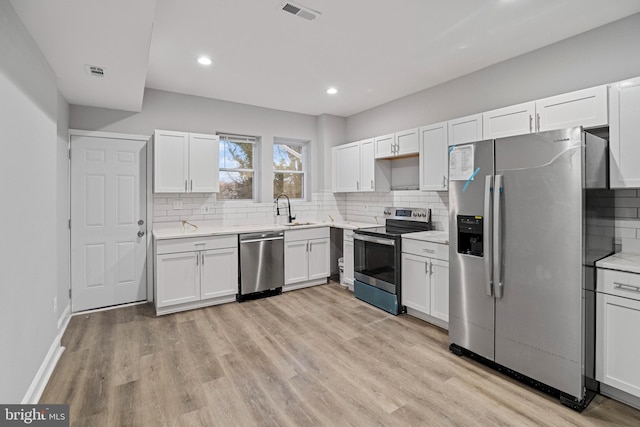 kitchen featuring light hardwood / wood-style floors, white cabinets, decorative backsplash, sink, and appliances with stainless steel finishes