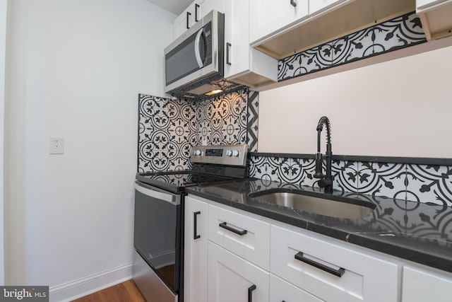 kitchen featuring white cabinets, backsplash, dark stone counters, sink, and stainless steel appliances