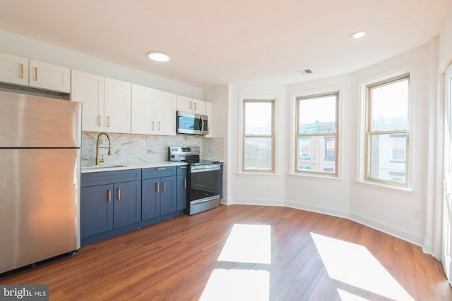 kitchen with appliances with stainless steel finishes, white cabinets, sink, and hardwood / wood-style floors