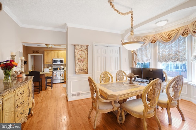 dining area featuring ceiling fan, a textured ceiling, light hardwood / wood-style flooring, and crown molding