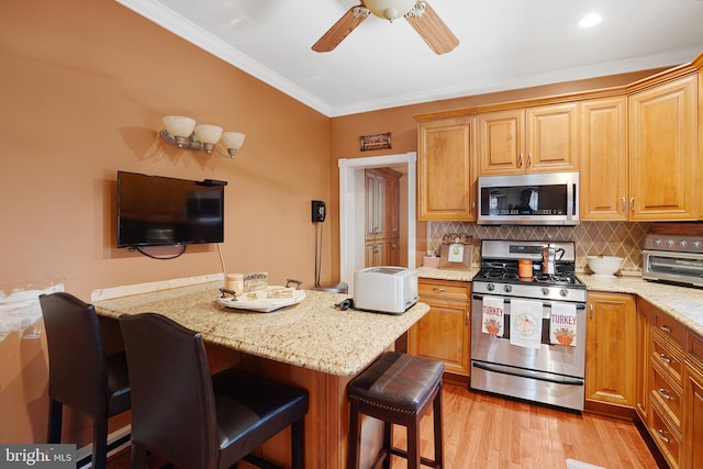 kitchen with light stone countertops, appliances with stainless steel finishes, a kitchen breakfast bar, and light hardwood / wood-style flooring