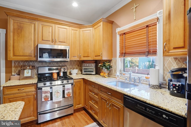 kitchen with tasteful backsplash, appliances with stainless steel finishes, light stone countertops, sink, and light hardwood / wood-style flooring