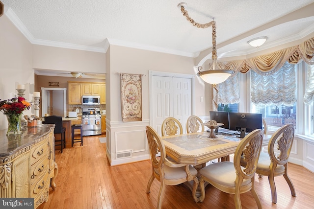 dining area with light wood-type flooring, a textured ceiling, and crown molding