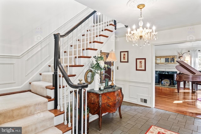 staircase featuring hardwood / wood-style flooring, ornamental molding, an inviting chandelier, and a fireplace