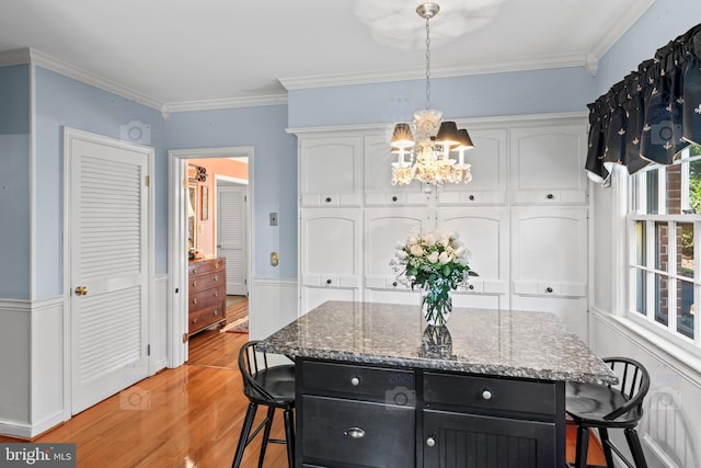 kitchen with a kitchen island, hanging light fixtures, white cabinetry, ornamental molding, and a breakfast bar area