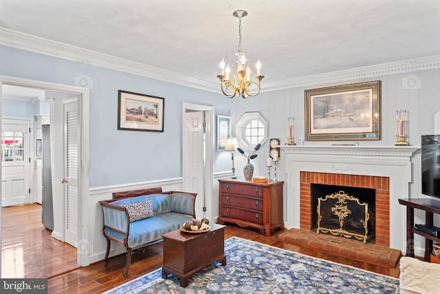 living area featuring ornamental molding, a chandelier, wood-type flooring, and a brick fireplace