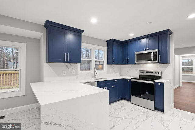 kitchen featuring blue cabinets, sink, plenty of natural light, light stone counters, and stainless steel appliances