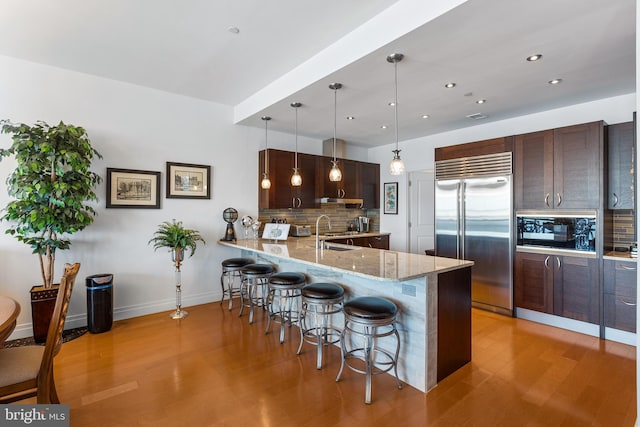 kitchen featuring built in appliances, kitchen peninsula, a breakfast bar area, decorative light fixtures, and light wood-type flooring