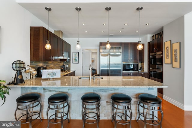 kitchen featuring backsplash, built in appliances, pendant lighting, and kitchen peninsula