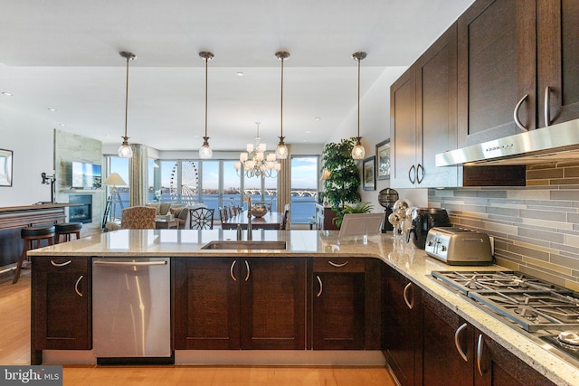 kitchen with light stone counters, stainless steel appliances, decorative light fixtures, an inviting chandelier, and light hardwood / wood-style floors