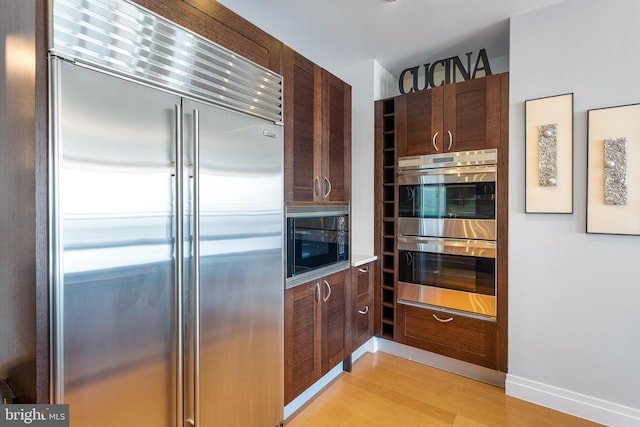 143 Waterfront St Unit 502, National Harbor, MD 20745 - kitchen with built in appliances, light wood-style floors, dark brown cabinets, and baseboards