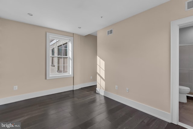 unfurnished bedroom with dark wood-style flooring, visible vents, baseboards, and ensuite bathroom