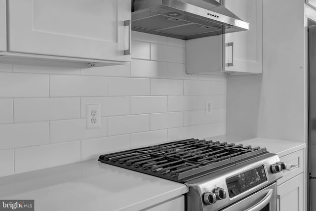 kitchen with decorative backsplash, white cabinetry, range hood, and gas range