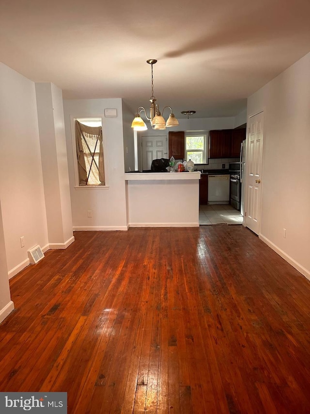 interior space featuring appliances with stainless steel finishes, kitchen peninsula, pendant lighting, a notable chandelier, and dark hardwood / wood-style floors