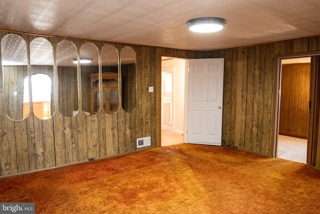 carpeted empty room featuring wood walls