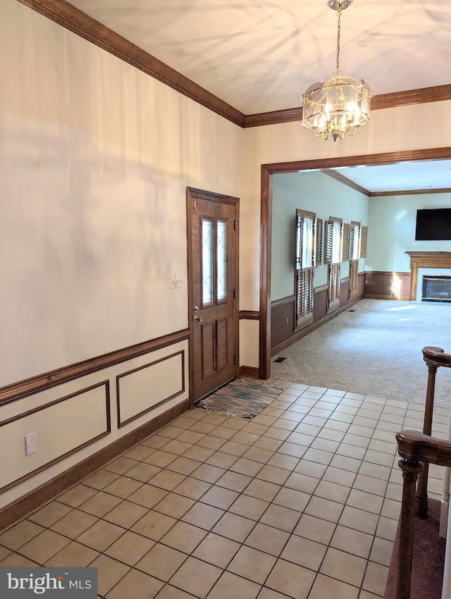 carpeted foyer featuring ornamental molding and a chandelier