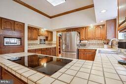 kitchen with ornamental molding, sink, tile countertops, and stainless steel refrigerator