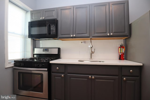 kitchen featuring decorative backsplash, stainless steel gas range oven, sink, and gray cabinets