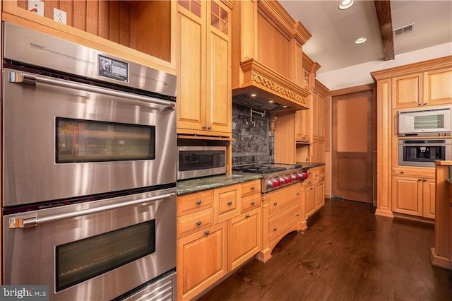 kitchen featuring decorative backsplash, appliances with stainless steel finishes, dark stone counters, custom range hood, and dark wood-type flooring