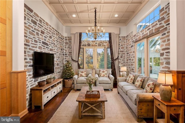 living room featuring an inviting chandelier, dark wood-type flooring, a high ceiling, crown molding, and coffered ceiling