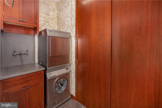 laundry area featuring cabinets, stacked washer and clothes dryer, and dark tile patterned flooring