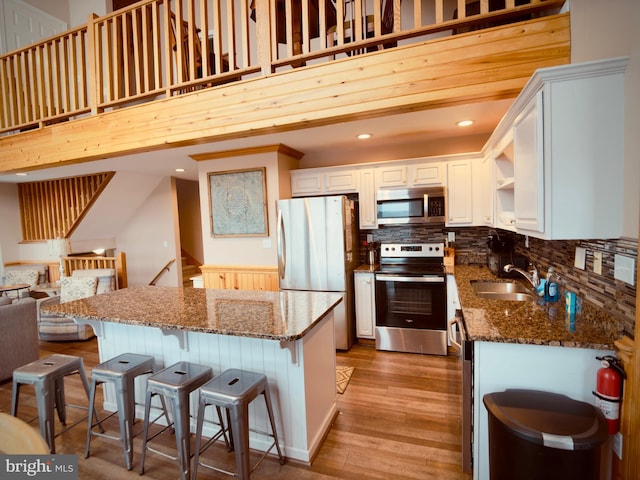 kitchen with stainless steel appliances, sink, light hardwood / wood-style flooring, dark stone countertops, and white cabinets