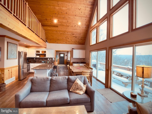 living room with light hardwood / wood-style flooring, a towering ceiling, and wooden ceiling