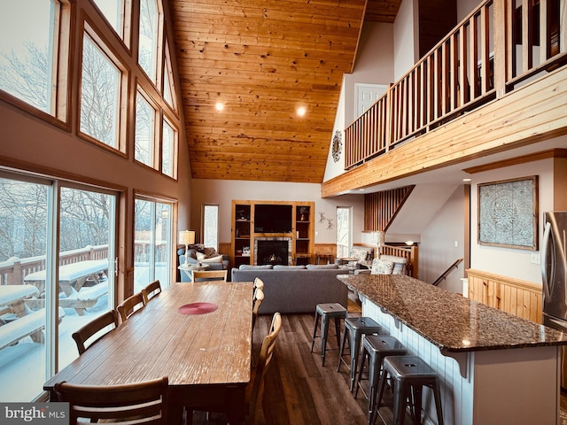 dining area with dark hardwood / wood-style flooring, a towering ceiling, a fireplace, and wood ceiling