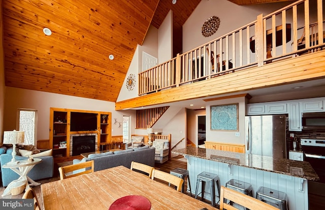 dining area featuring a fireplace, high vaulted ceiling, and wooden ceiling