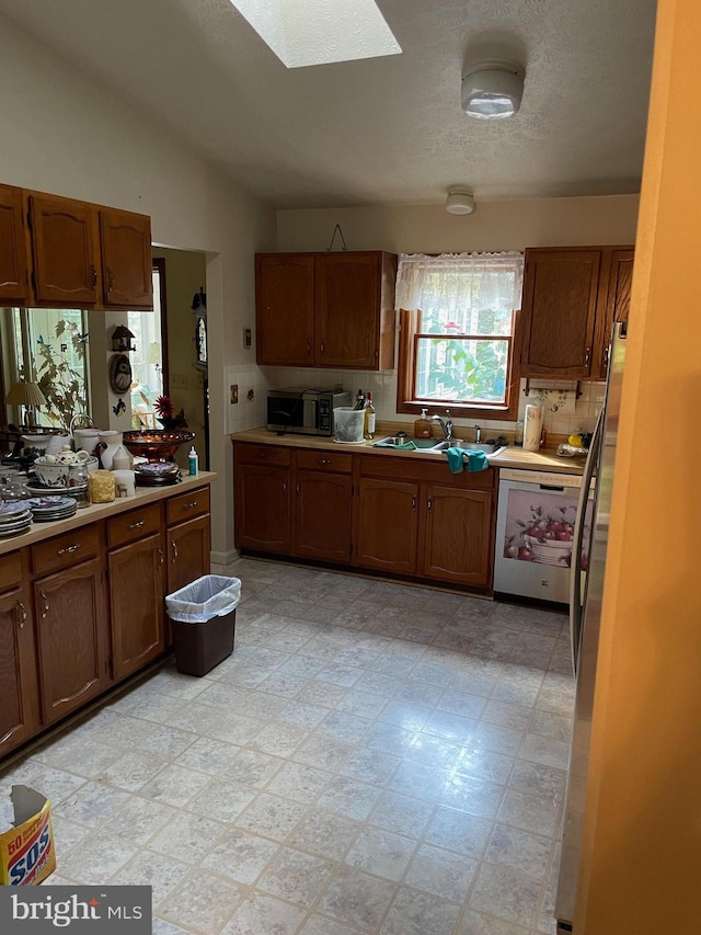 kitchen with lofted ceiling with skylight, sink, decorative backsplash, and stainless steel appliances