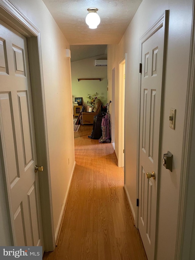 hall featuring light hardwood / wood-style floors, a textured ceiling, and a wall mounted air conditioner