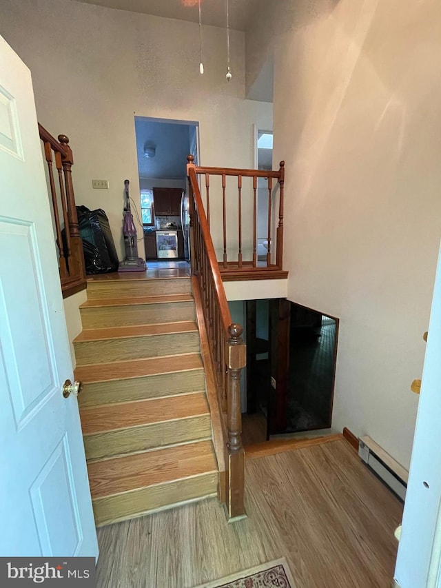 staircase featuring a baseboard heating unit and hardwood / wood-style flooring