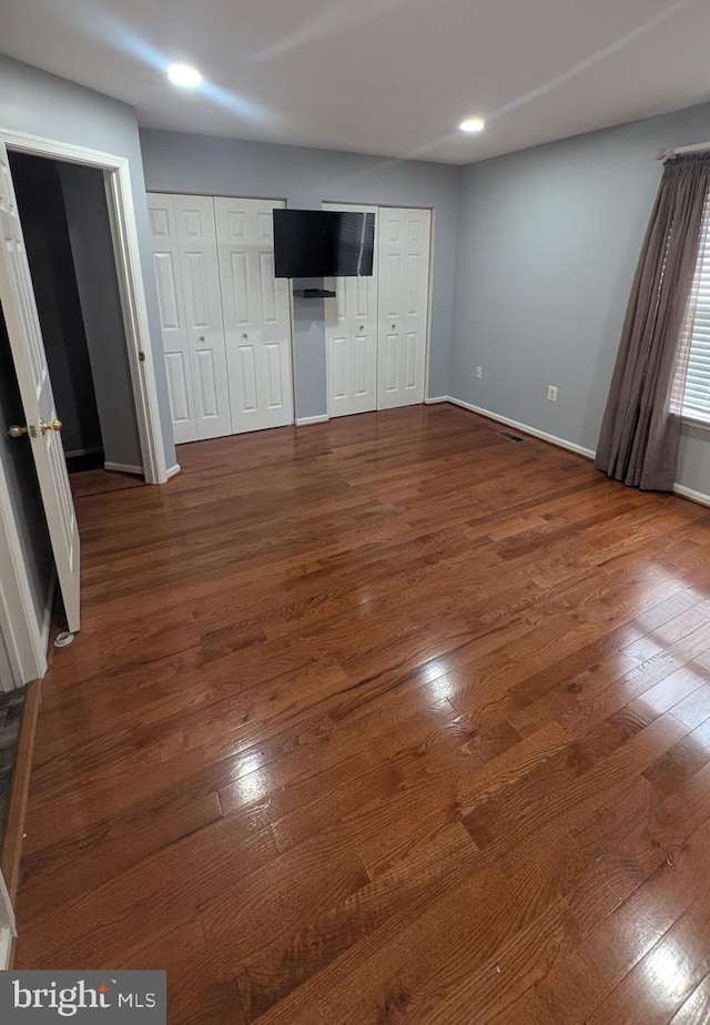 unfurnished bedroom with dark hardwood / wood-style floors and two closets