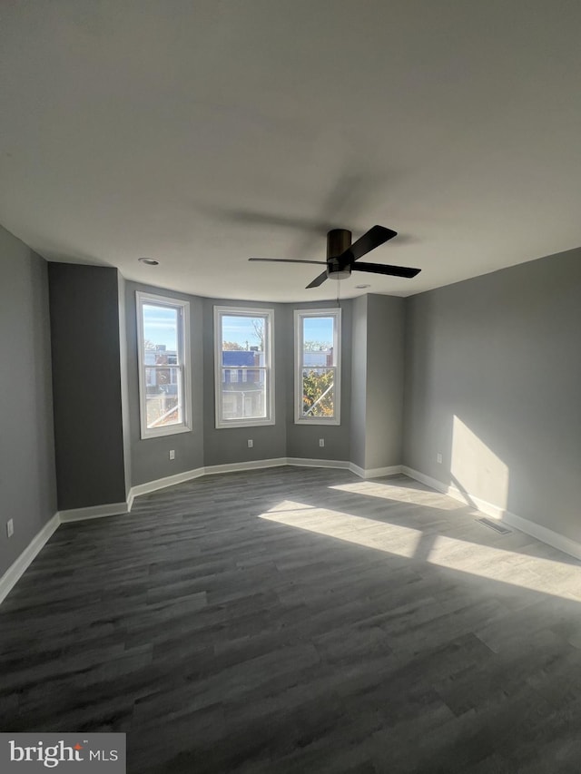 empty room with dark wood-type flooring, a healthy amount of sunlight, and ceiling fan